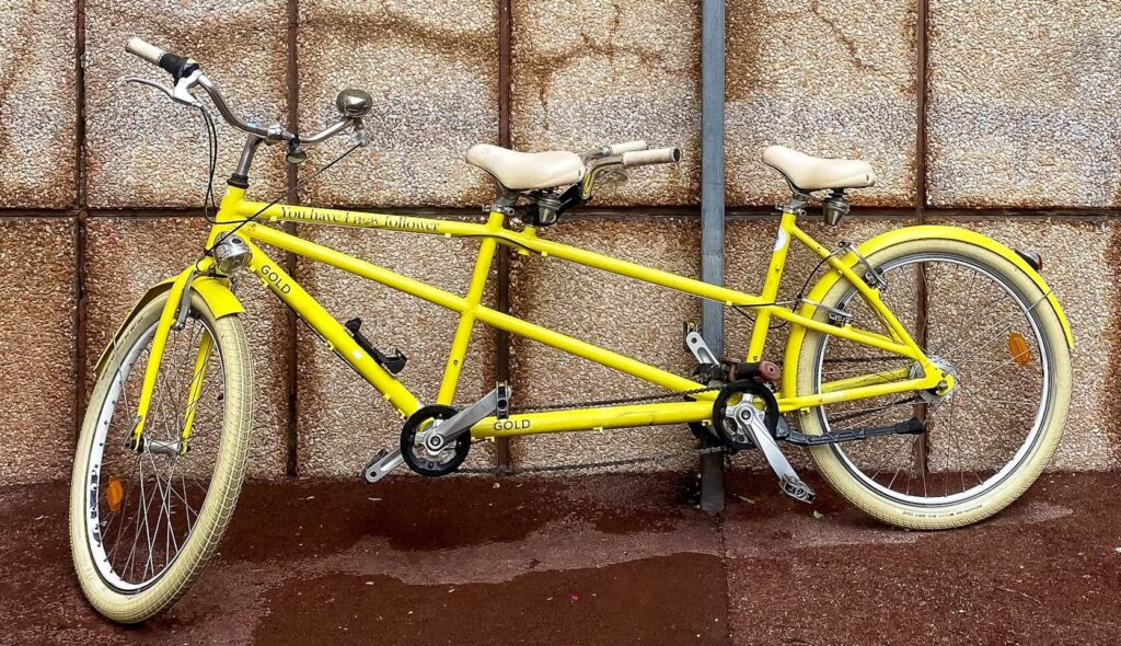 Foto eines gelben Tandems das an einer Wand angelehnt ist.